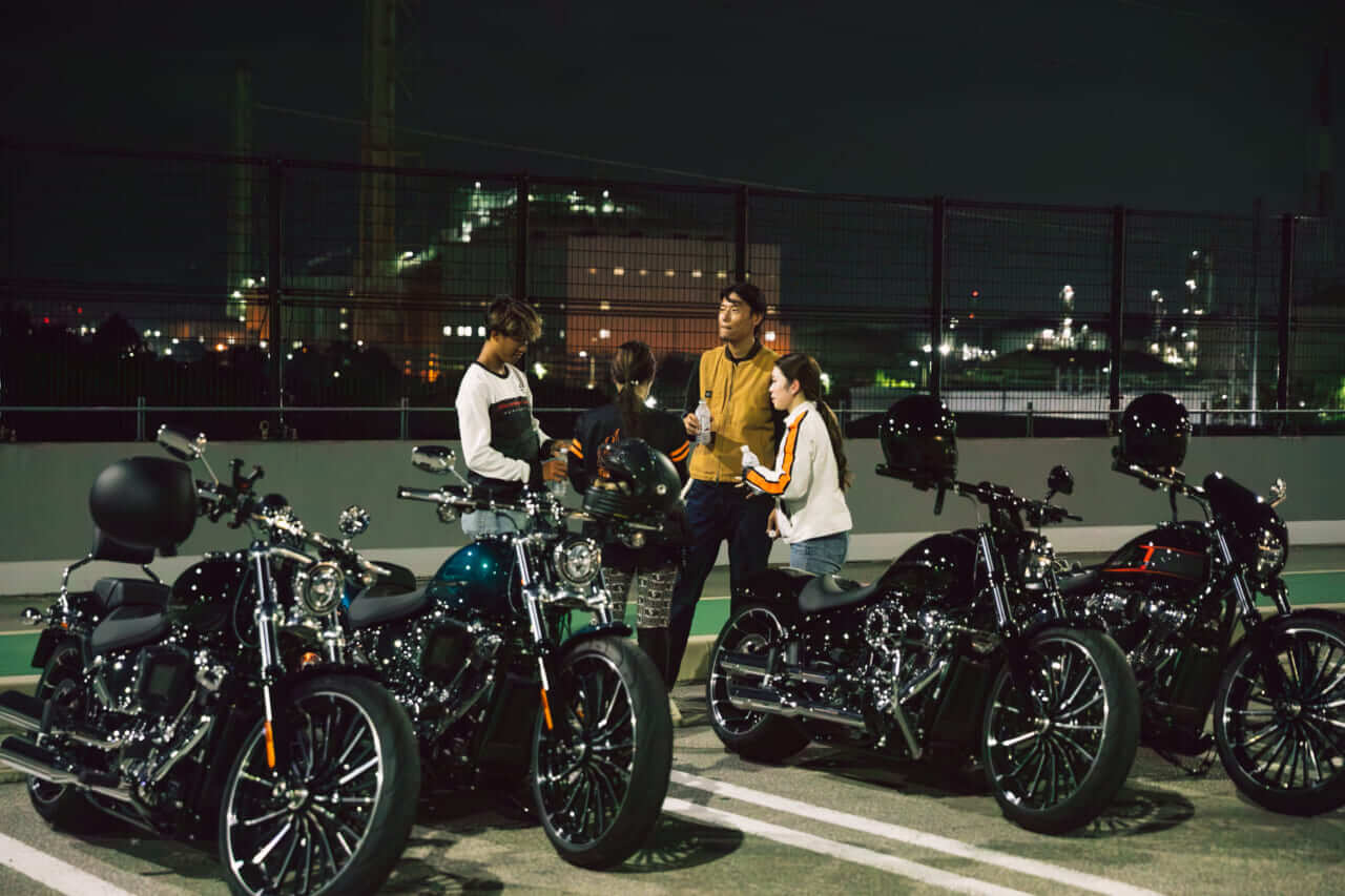 กลุ่มคนขี่พูดคุยข้างรถ Harley-Davidson Breakout ในช่วงค่ำ